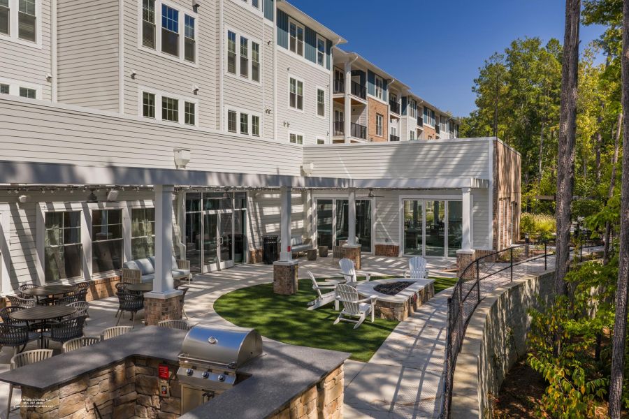 Acclaim at Cary Pointe apartment homes with Outdoor patio with seating, fire pit, grill, and modern apartment building in the background on a sunny day.