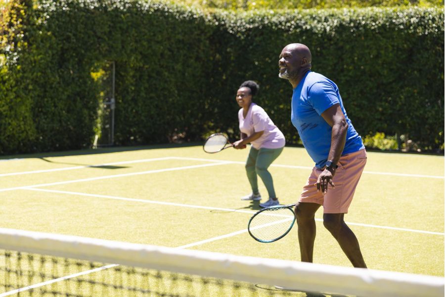 Attain on 5th apartment homes with Two people playing doubles tennis outdoors, ready at the net with rackets, on a sunny day.