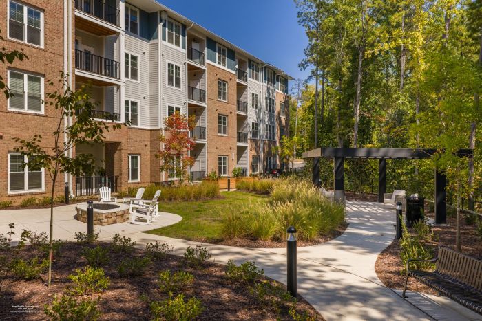 Acclaim at Cary Pointe apartment homes with Modern apartment building with balconies, outdoor seating, fire pit, walkway, and landscaped garden.