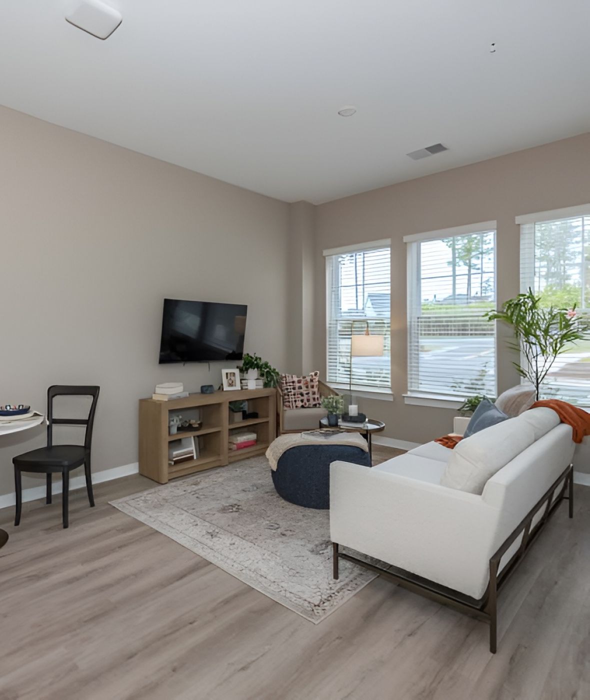 Acclaim at Cary Pointe apartment homes with Modern living room with a white sofa, TV, small dining table, and large windows letting in natural light.