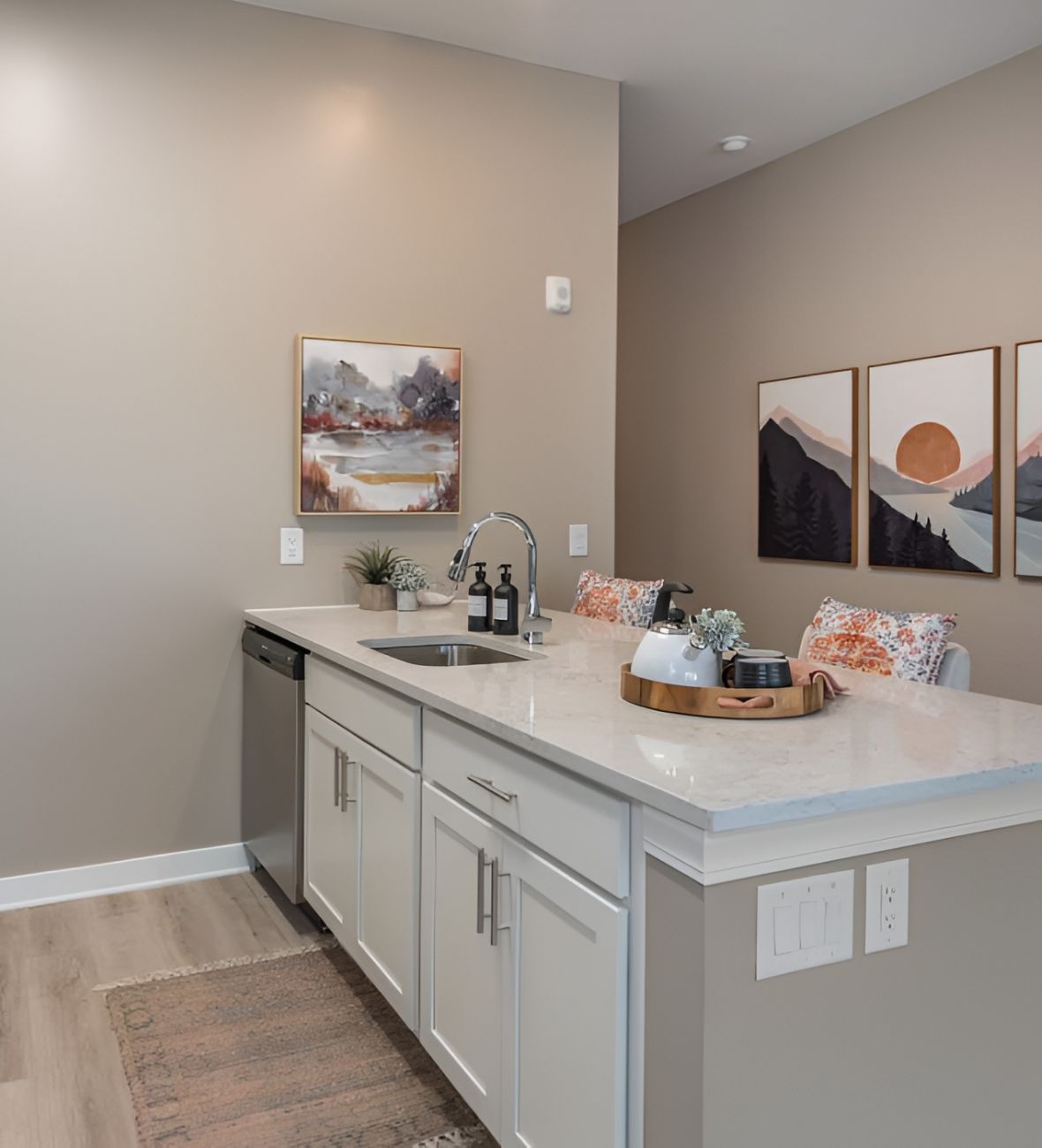 Acclaim at Cary Pointe apartment homes with Modern kitchen with white cabinets, island sink, decor items, and landscape art on neutral tan walls.