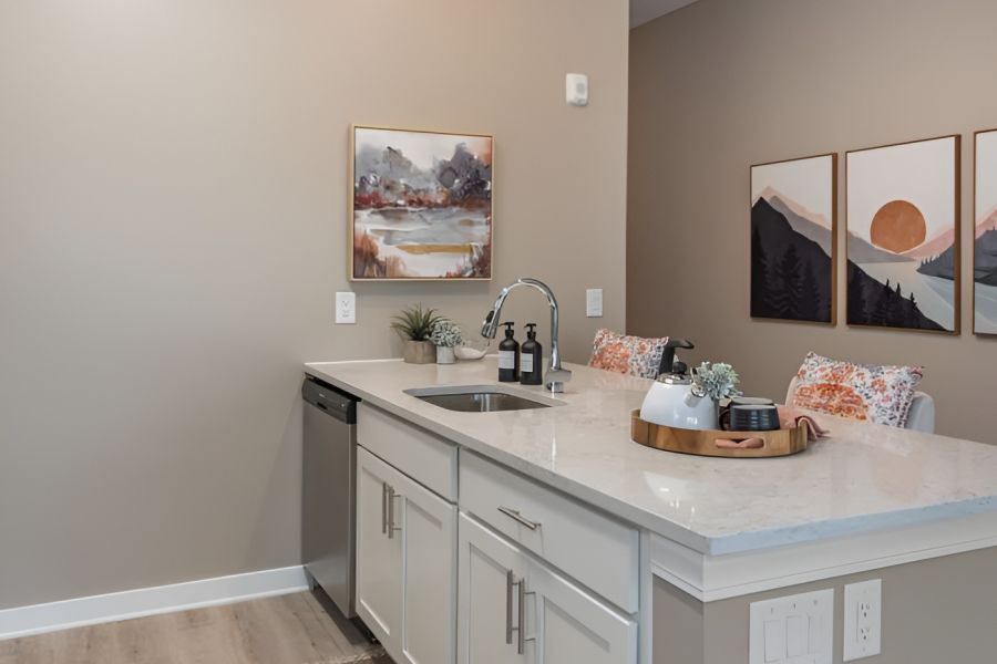 Acclaim at Cary Pointe apartment homes with Modern kitchen with white cabinets, island sink, decor items, and landscape art on neutral tan walls.