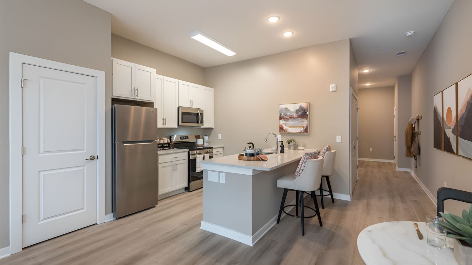 Modern kitchen and living area with white cabinets, stainless steel appliances, and a large island. Cozy seating area with a sofa and rug in the background. Bright and inviting atmosphere.