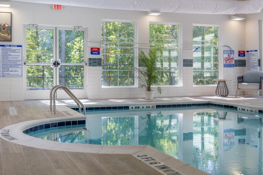 Acclaim at Cary Pointe apartment homes with Indoor swimming pool with clear water, surrounded by windows, a plant, and pool safety signs on the walls.