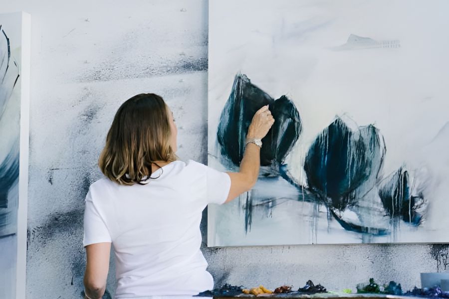 Acclaim at Cary Pointe apartment homes with A person in a white shirt paints an abstract artwork in blue and black on a canvas in a studio.