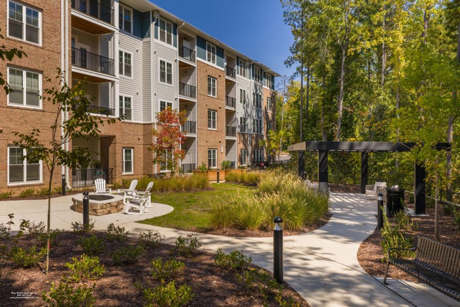 Acclaim at Cary Pointe apartment homes with Modern apartment building with balconies, outdoor seating, fire pit, walkway, and landscaped garden.