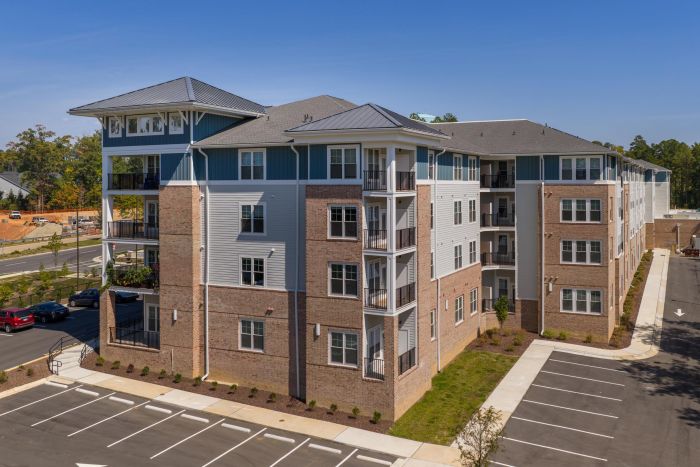 Acclaim at Cary Pointe apartment homes with Four-story modern apartment building with balconies and adjacent empty parking lot on a sunny day.