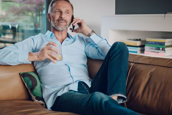 Acclaim at Cary Pointe homes with Man relaxing on a couch, talking on the phone and holding a drink, with books and a window in the background.