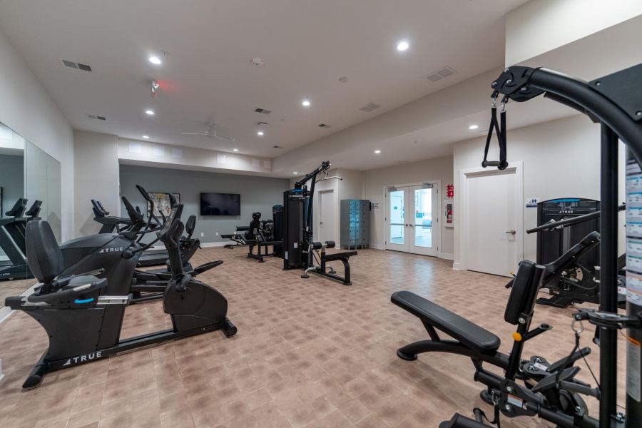 Acclaim at Cary Pointe apartment homes with Modern gym with exercise bikes, weight machines, benches, and a TV on the wall in a bright, spacious room.