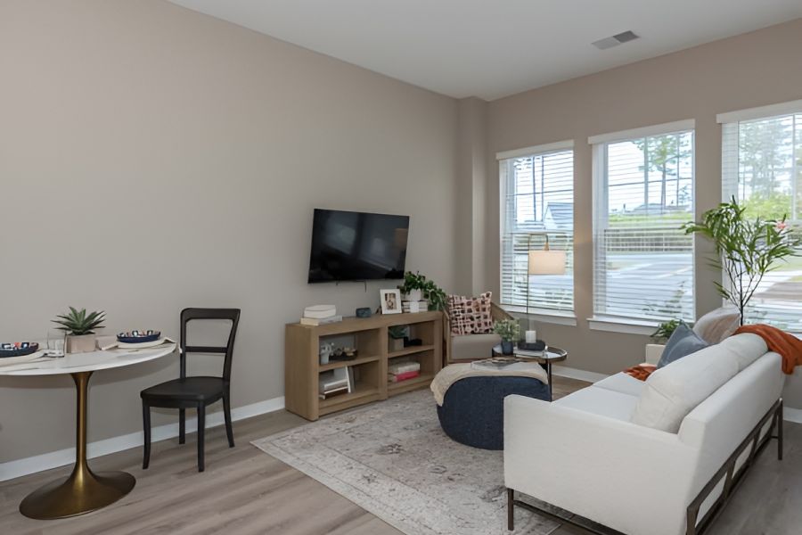 Acclaim at Cary Pointe apartment homes with Modern living room with a white sofa, TV, small dining table, and large windows letting in natural light.