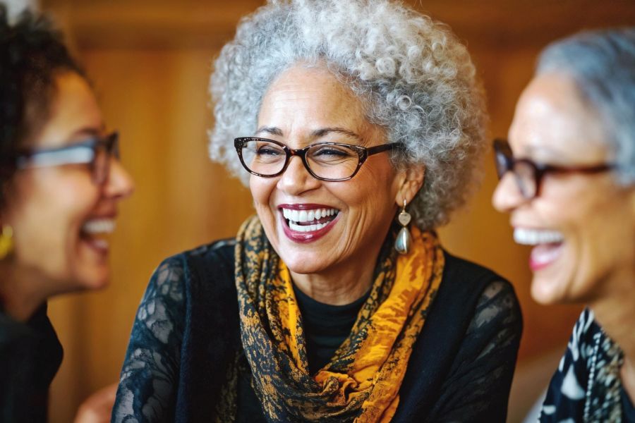 Attain on 5th apartment homes with Three older women with glasses laughing and talking together, one wearing a yellow scarf, indoors.