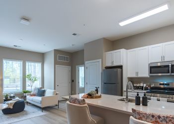 Acclaim at Cary Pointe apartment homes with Modern open-plan kitchen and living room with white cabinets, bar stools, and large windows.