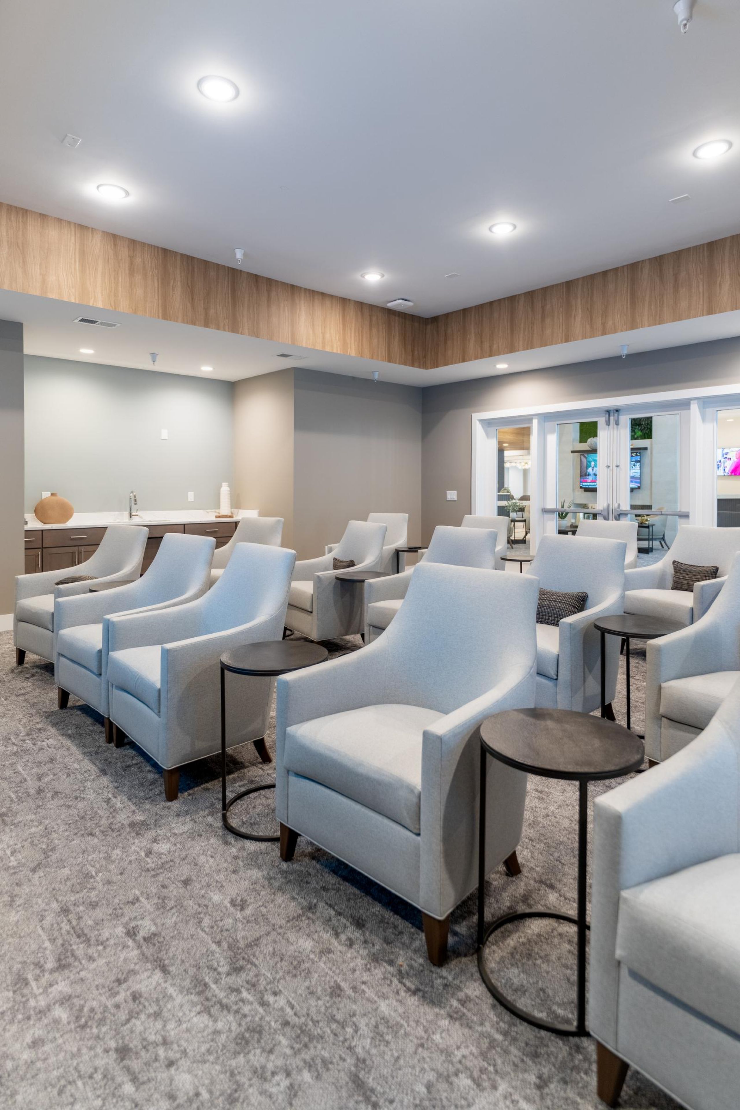 Acclaim at Cary Pointe apartment homes with Modern lounge with rows of light gray armchairs and round side tables on a gray carpeted floor.