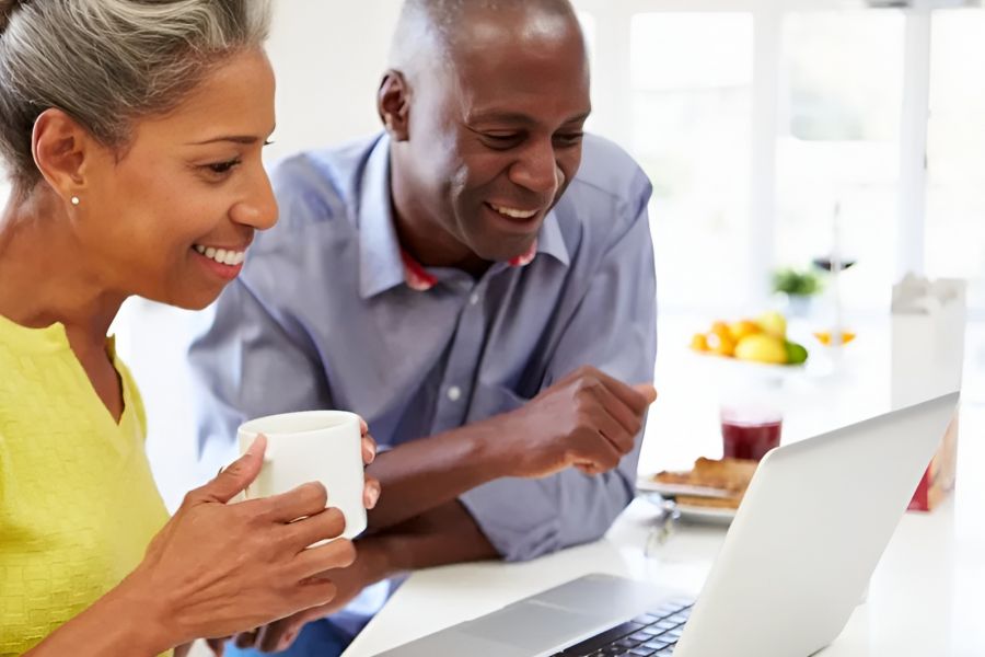 Acclaim at Cary Pointe apartment homes with Smiling couple using a laptop together in a bright kitchen; the woman holds a white mug.