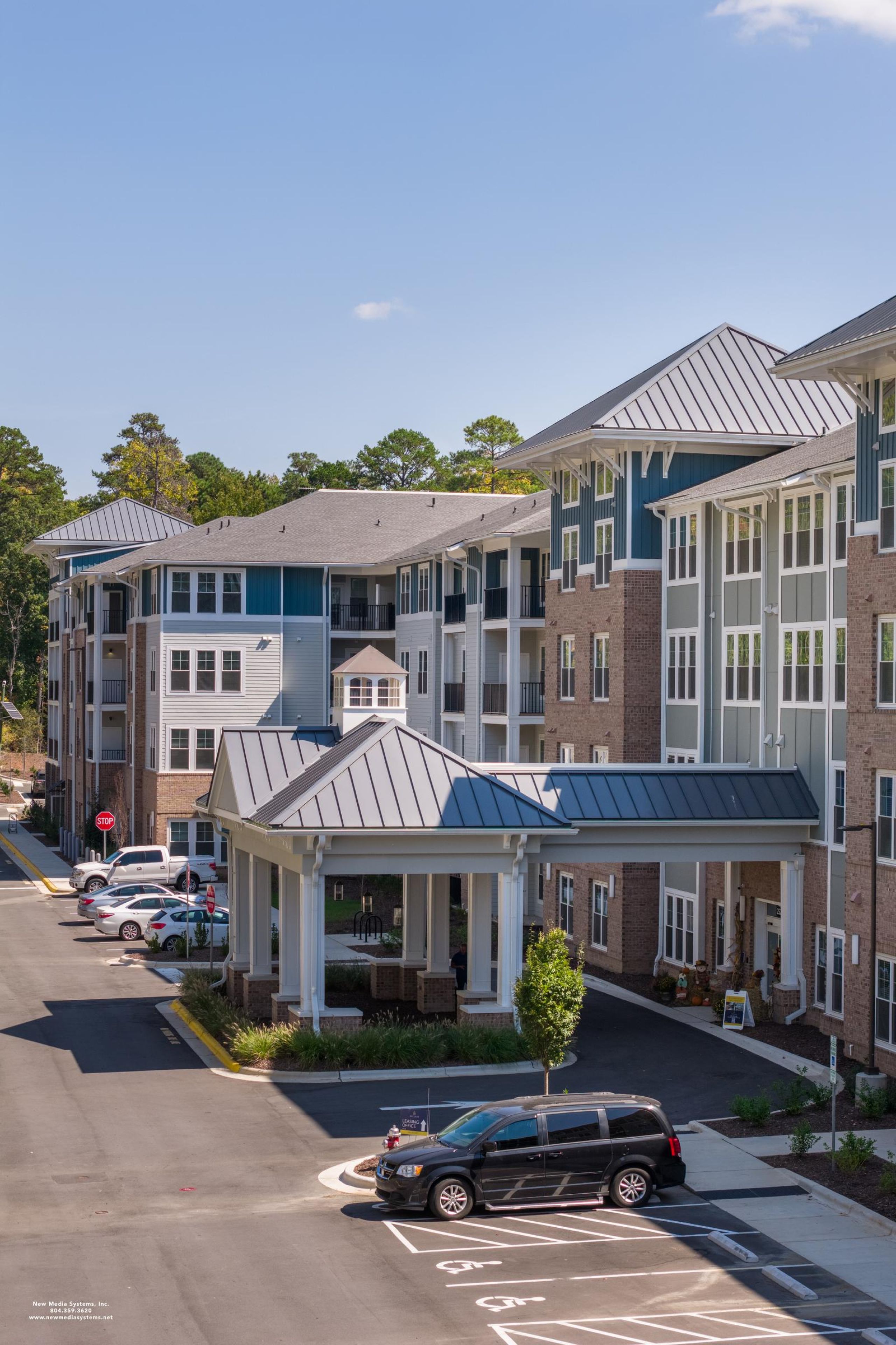 Acclaim at Cary Pointe  apartment homes with Modern multi-story apartment complex with parked cars, a covered entrance, and clear blue sky above.