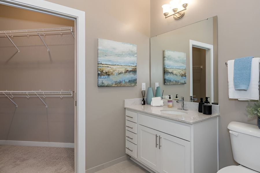 Acclaim at Cary Pointe apartment homes with Modern bathroom with a large mirror, white vanity, and an open walk-in closet with empty shelves.