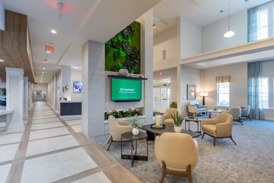 Acclaim at Cary Pointe apartment homes with Modern lobby with beige chairs, small tables, a green wall, and a digital screen above a fireplace.