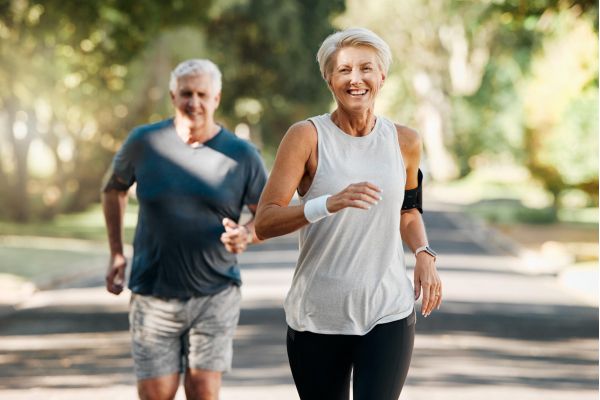 Attain on 5th apartment homes with Older man and woman jogging outdoors on a sunny day, both smiling and dressed in athletic wear.
