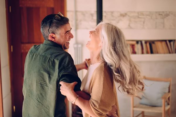 Acclaim at Cary Pointe apartment homes with An older couple dances and laughs together in a cozy, sunlit living room.