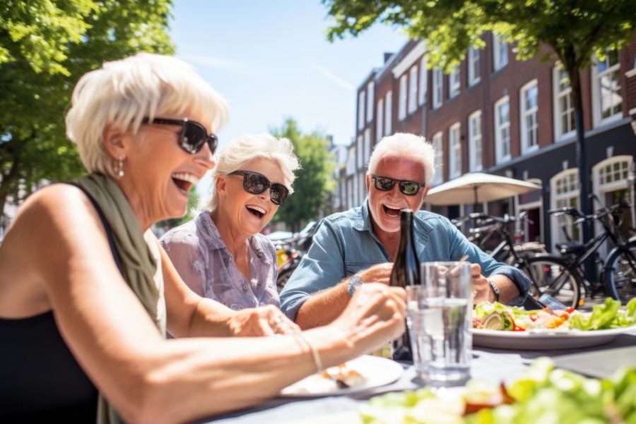 Attain on 5th apartment homes with Three smiling older adults wearing sunglasses laugh together while dining outside on a sunny day.