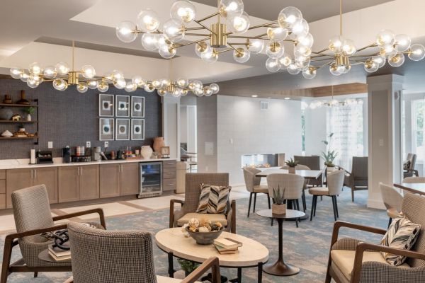 Acclaim at Cary Pointe apartment homes with Modern lounge with armchairs, round tables, a kitchenette, large windows, and decorative chandeliers overhead.