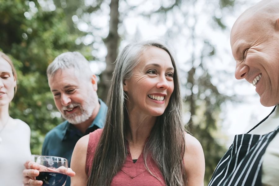 Acclaim at Cary Pointe apartment homes with Four adults smiling and talking outdoors, one holding a drink, with trees in the background.
