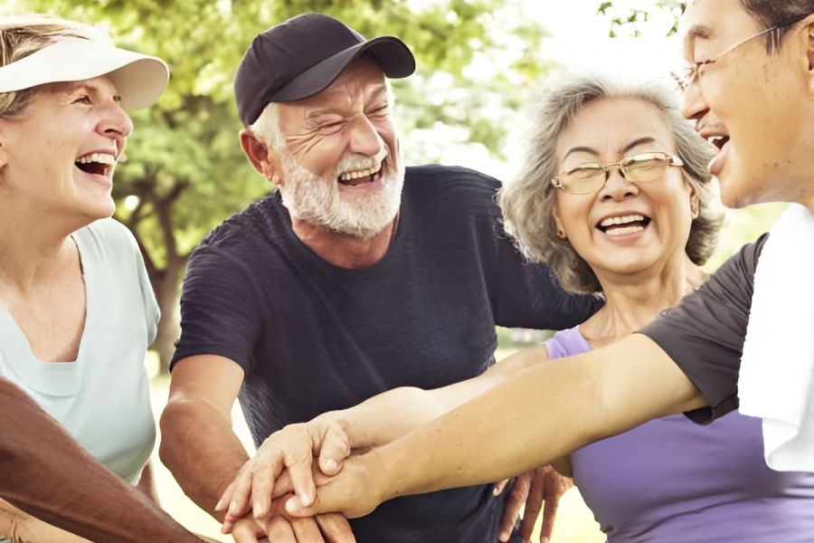 Acclaim at Cary Pointe apartment homes with A group of happy seniors laughing and stacking hands together outdoors in a park.