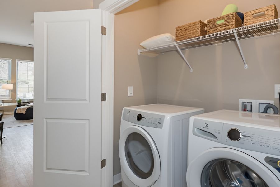 Acclaim at Cary Pointe apartment homes with Laundry room with front-loading washer, dryer, open door, and shelves holding baskets and linens.
